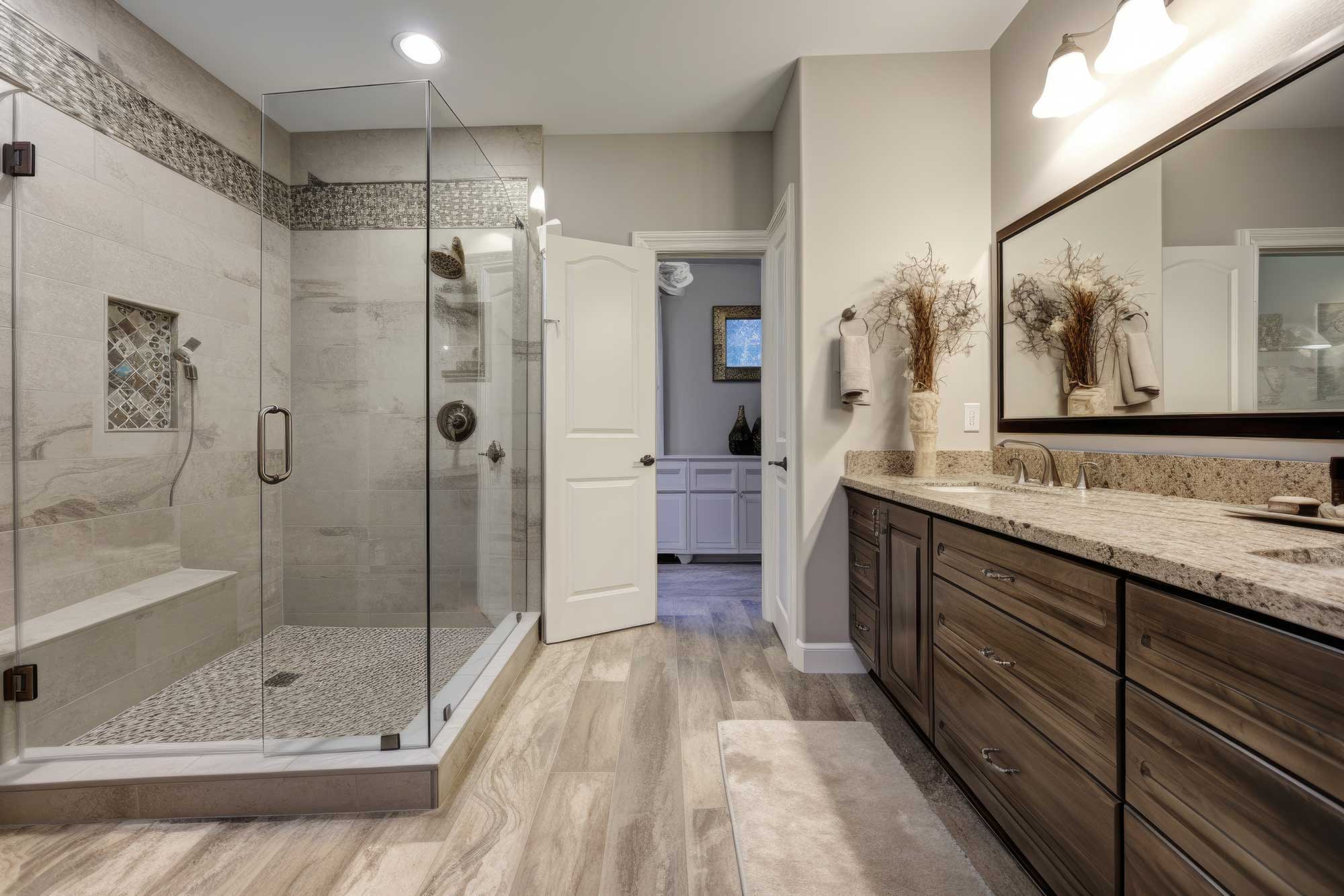 Remodelled bathroom with a glass corner shower, granite-topped double vanity and wood-look plank flooring