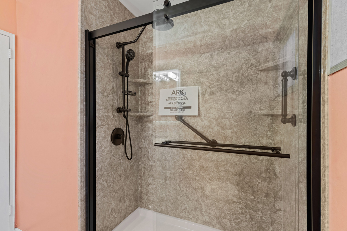 Tub-to-shower conversion finished with stone-look walls, a corner shelf and bronze fixtures