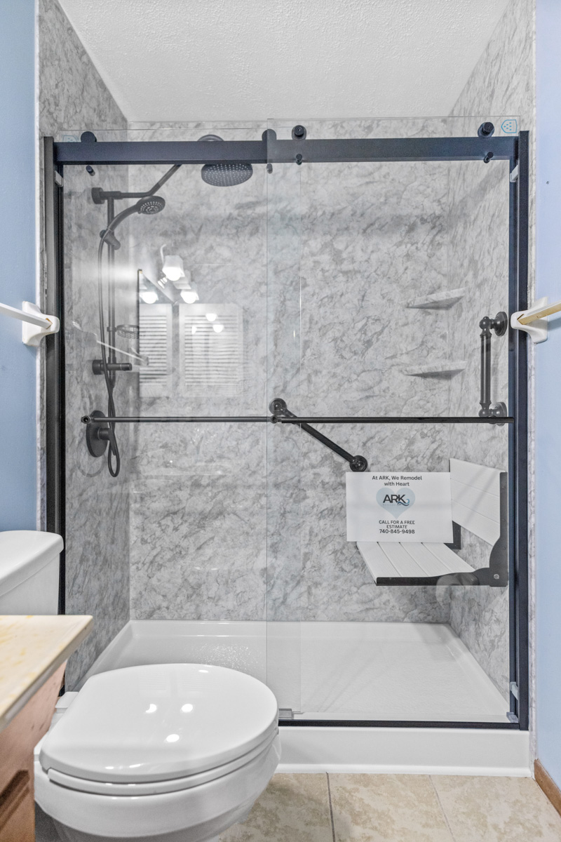 Accessible walk-in shower with a fold-down seat, grab bar and marble-look wall panels