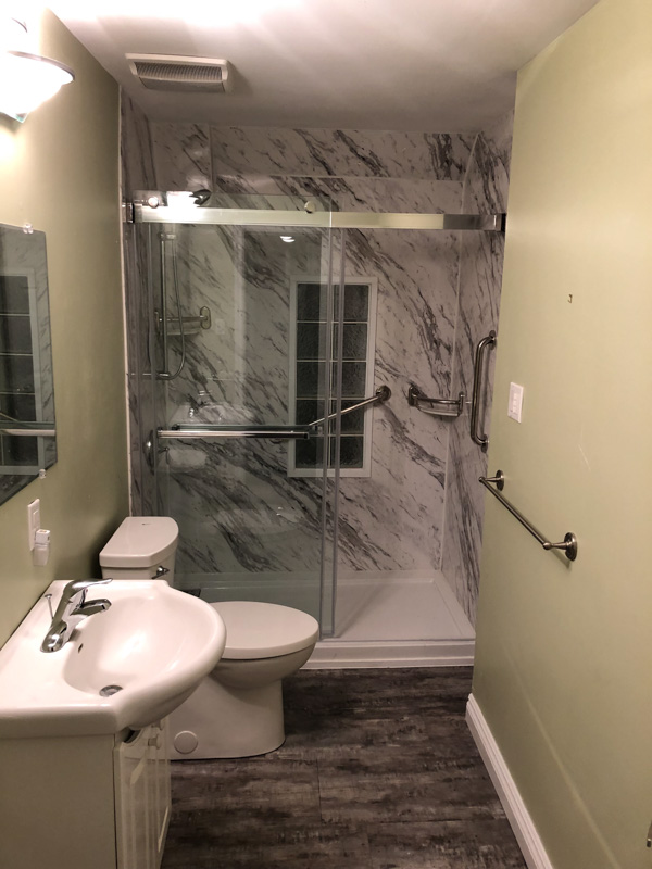 Marble-look walk-in shower with sliding glass doors and chrome grab bars