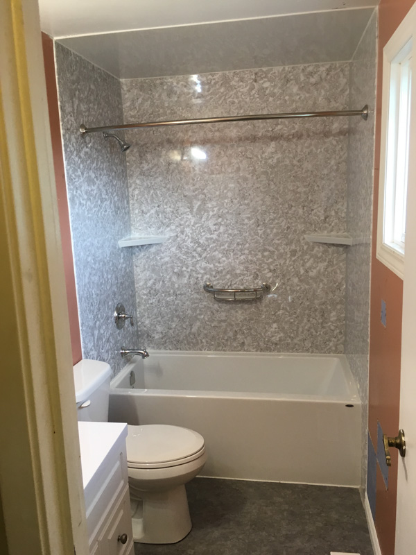 New white bathtub with a grey marbled wall surround, moulded corner shelves and a chrome grab bar