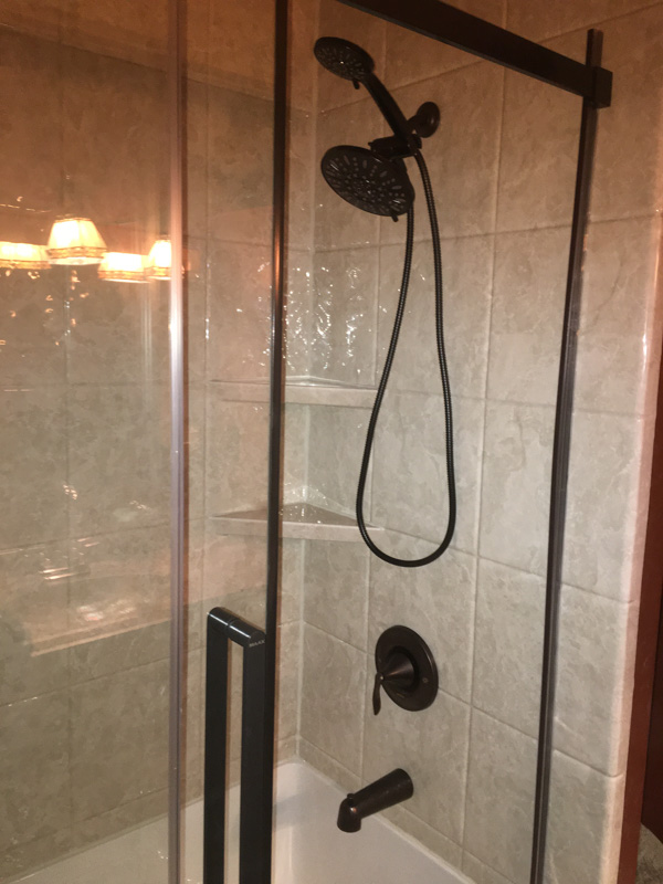 Shower with travertine-look wall panels and oil-rubbed bronze fixtures behind a framed glass door