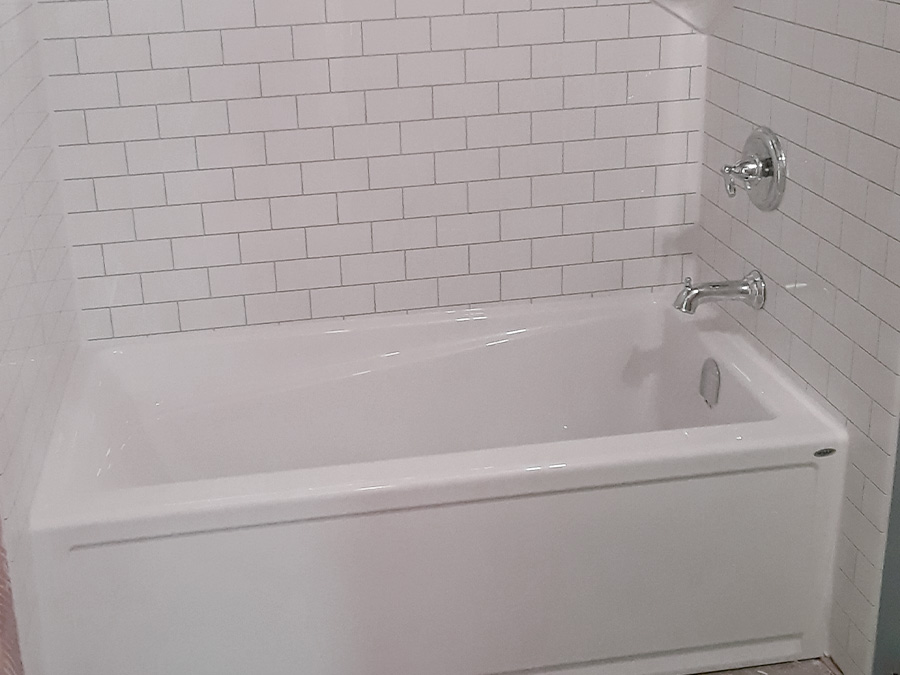 New white alcove bathtub with a white subway tile surround and chrome fixtures