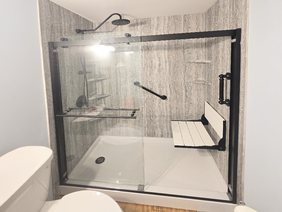 Walk-in shower with stone-look wall panels, a folding bench seat and a matte black sliding door