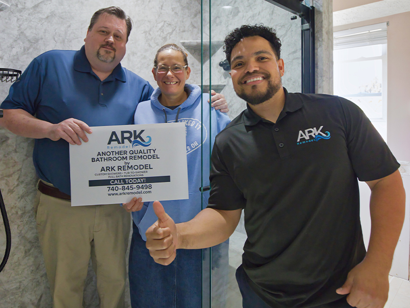 ARK Remodel installers with a homeowner in front of a finished shower, holding an ARK Remodel sign